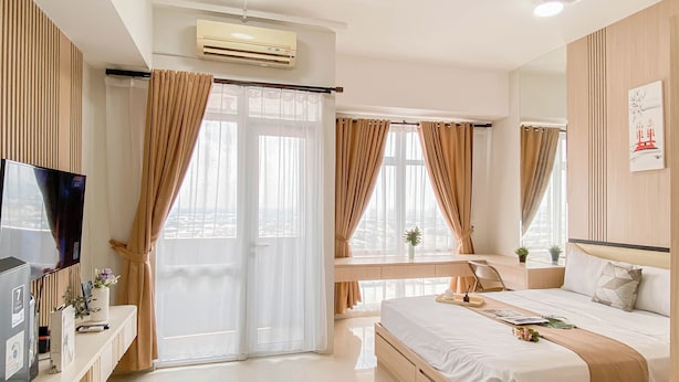 A modern hotel room with a large bed, a desk, a TV, and a window with curtains. - 1Br At Apartment Vasanta Innopark Near Mm2100 Area (Cikarang)