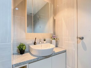 A modern bathroom with a white sink, a mirror, and a potted plant.