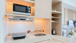 A modern kitchen with a microwave, stove, and sink. There are wooden cabinets and a countertop. - 1Br At Apartment Vasanta Innopark Near Mm2100 Area (Cikarang)