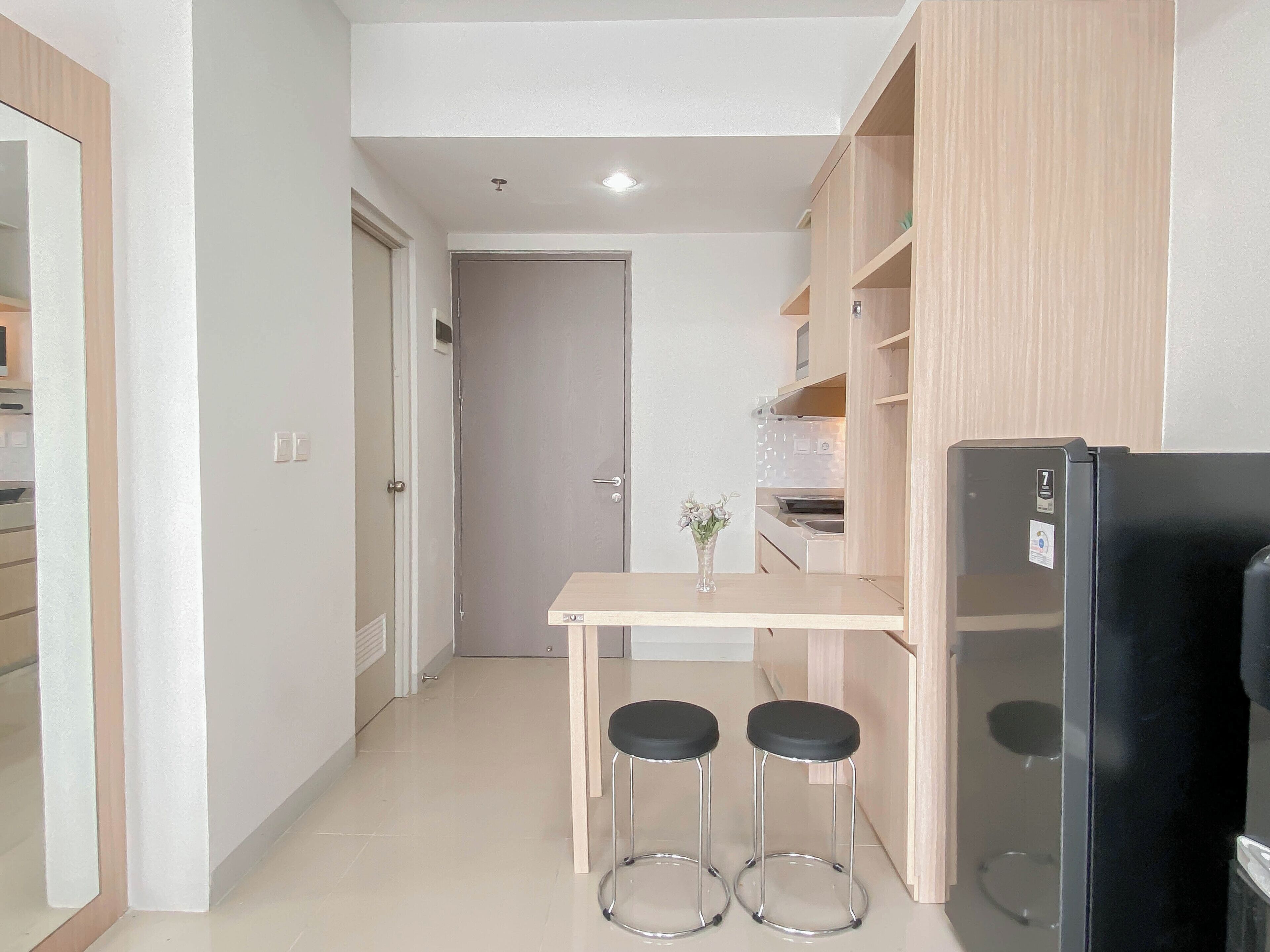 A small kitchenette with a black refrigerator, a wooden cabinet, and a table with two stools.