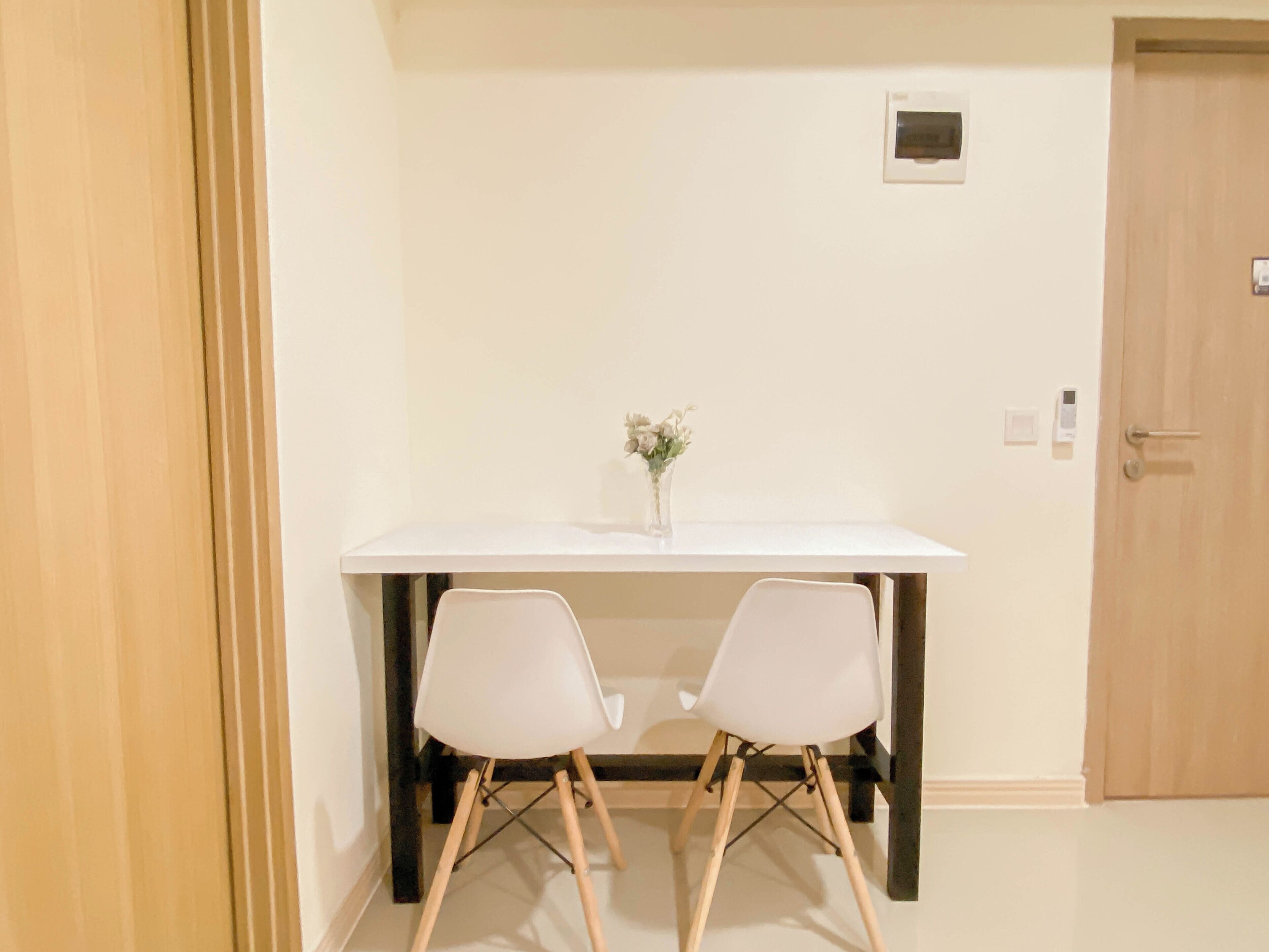 A room with a white table, two white chairs, a vase with flowers, and a wooden door.