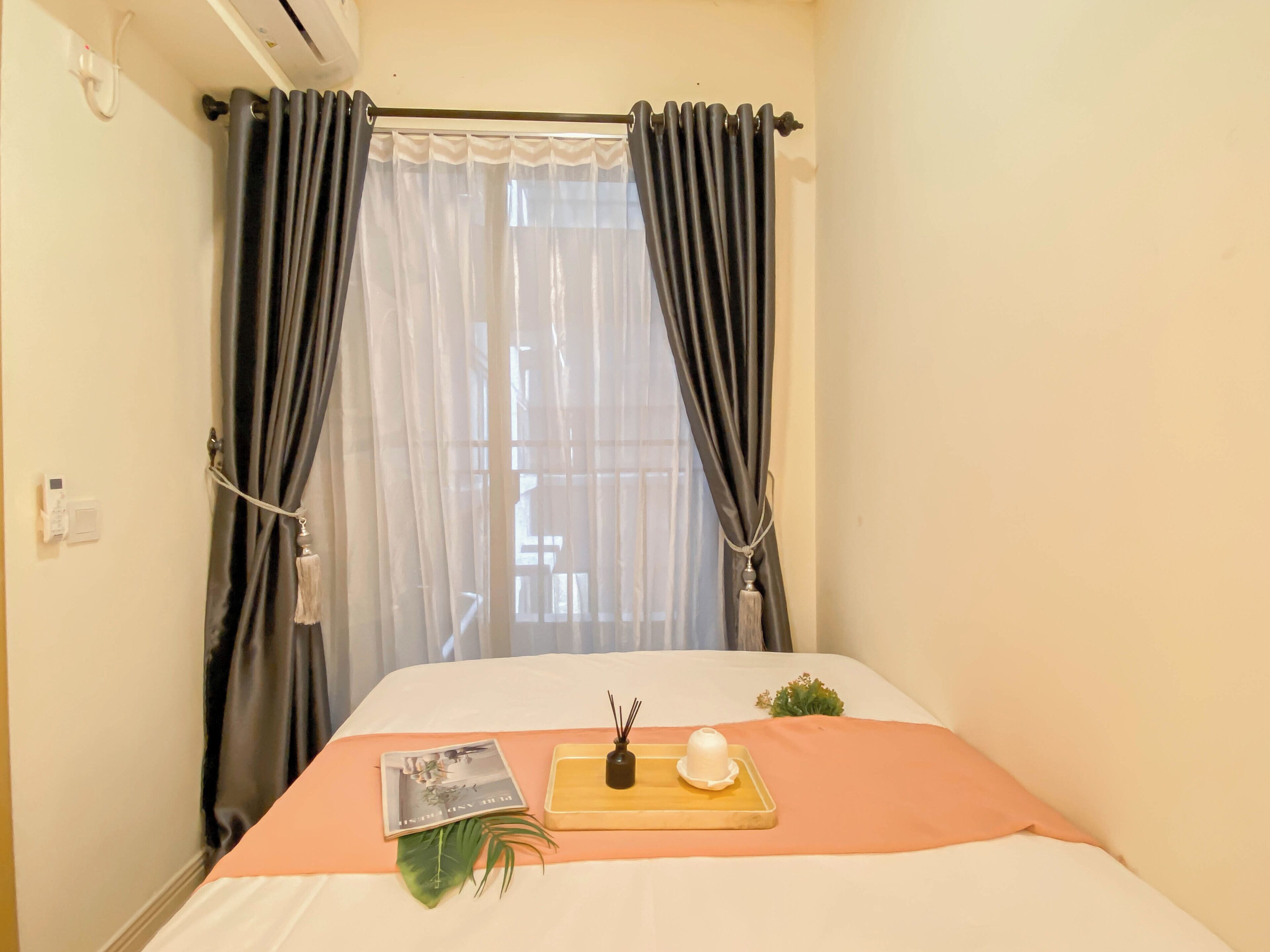 A neatly made bed with a magazine, a small plant, and a tray with a candle and a bowl.