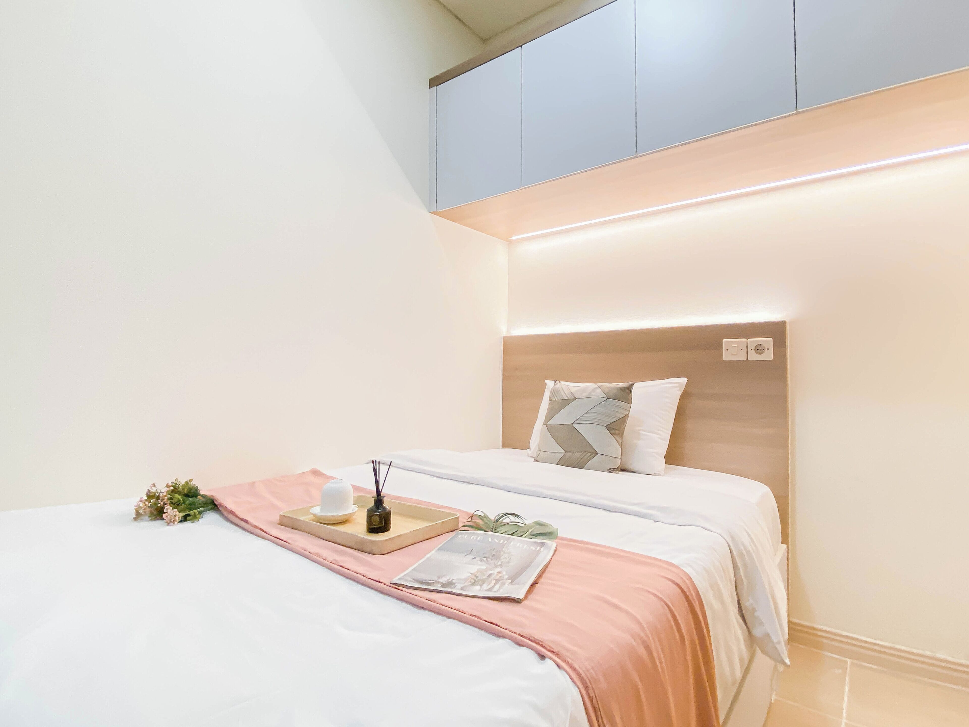 A neatly made bed with a pink blanket, a tray with a candle and flowers, and a pillow with a geometric pattern.