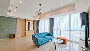 A spacious living room with a blue sofa, a round coffee table, and a modern chandelier. - Modern And Spacious 3Br At Apartment Hillcrest House (Curug)
