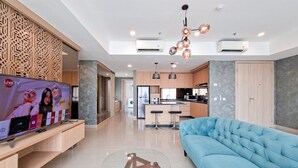 A modern living room with a television, a glass coffee table, and a blue sofa. - Modern And Spacious 3Br At Apartment Hillcrest House (Curug)