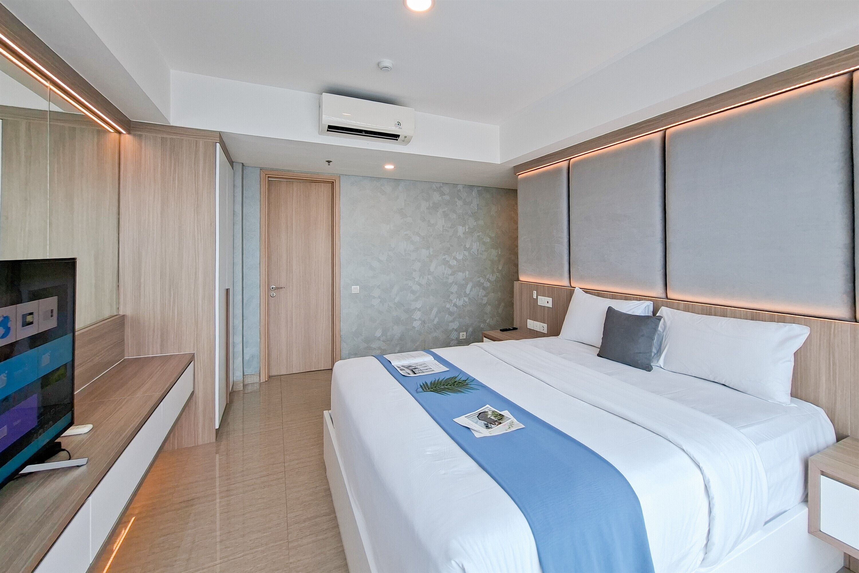 A modern hotel room with a large bed, a flat-screen TV, and a built-in air conditioning unit.