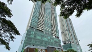 A modern high-rise building with reflective glass windows and a commercial ground floor. - Modern And Spacious 3Br At Apartment Hillcrest House (Curug)