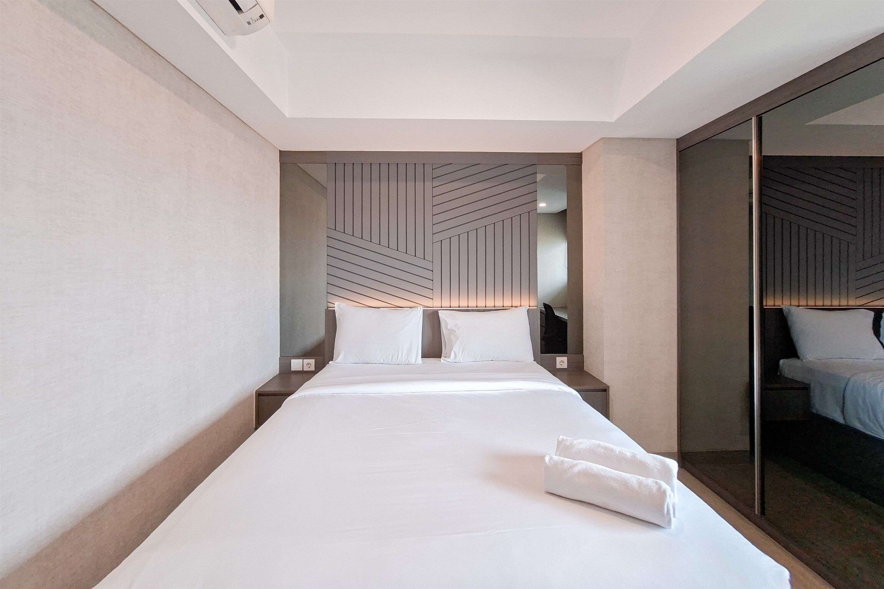 A modern hotel room with a large bed, a nightstand, a mirror, and a geometric-patterned headboard.