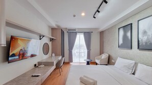 Una habitación de hotel con cama, escritorio, televisor, silla y una mesita.