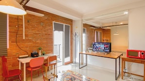 A modern living room with a TV, red chairs, a white table, and a patterned rug. - Spacious Studio At Signature Park Grande Apartment (Jakarta)