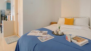 A bedroom with a bed, a bedside table, a nightstand, and a window. - Spacious Studio At Signature Park Grande Apartment (Jakarta)