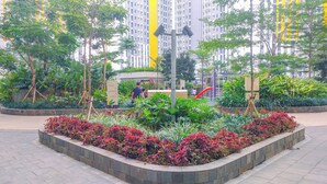 A landscaped urban area with a central garden, a playground, and a tall building in the background. - Strategic Studio At Apartment Springlake Summarecon Bekasi (Bekasi)