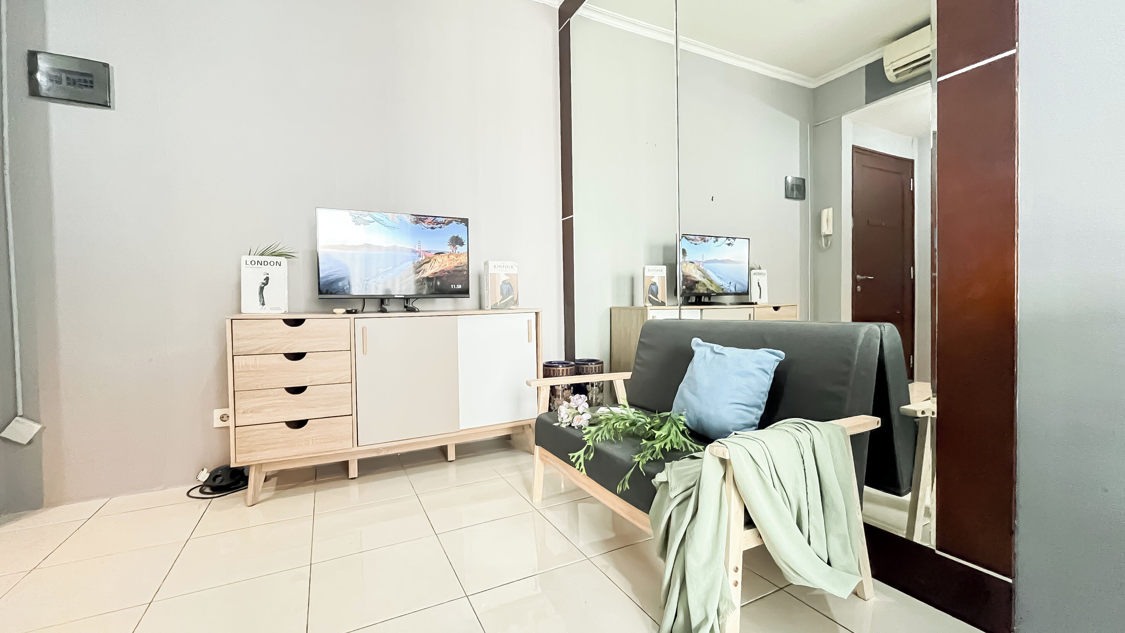 Ett modernt vardagsrum med en grå soffa, ett träskåp med lådor, en platt-TV och ett litet sidobord med en växt.