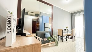 A modern living room with a sofa, a coffee table, and a dining area with chairs. There is a kitchen visible in the background. - Cozy And Modern 2Br Apartment Marina Ancol (Jakarta)