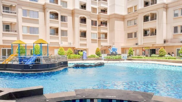 A swimming pool with a children's play area, surrounded by a multi-story building with balconies. - Cozy And Modern 2Br Apartment Marina Ancol (Jakarta)
