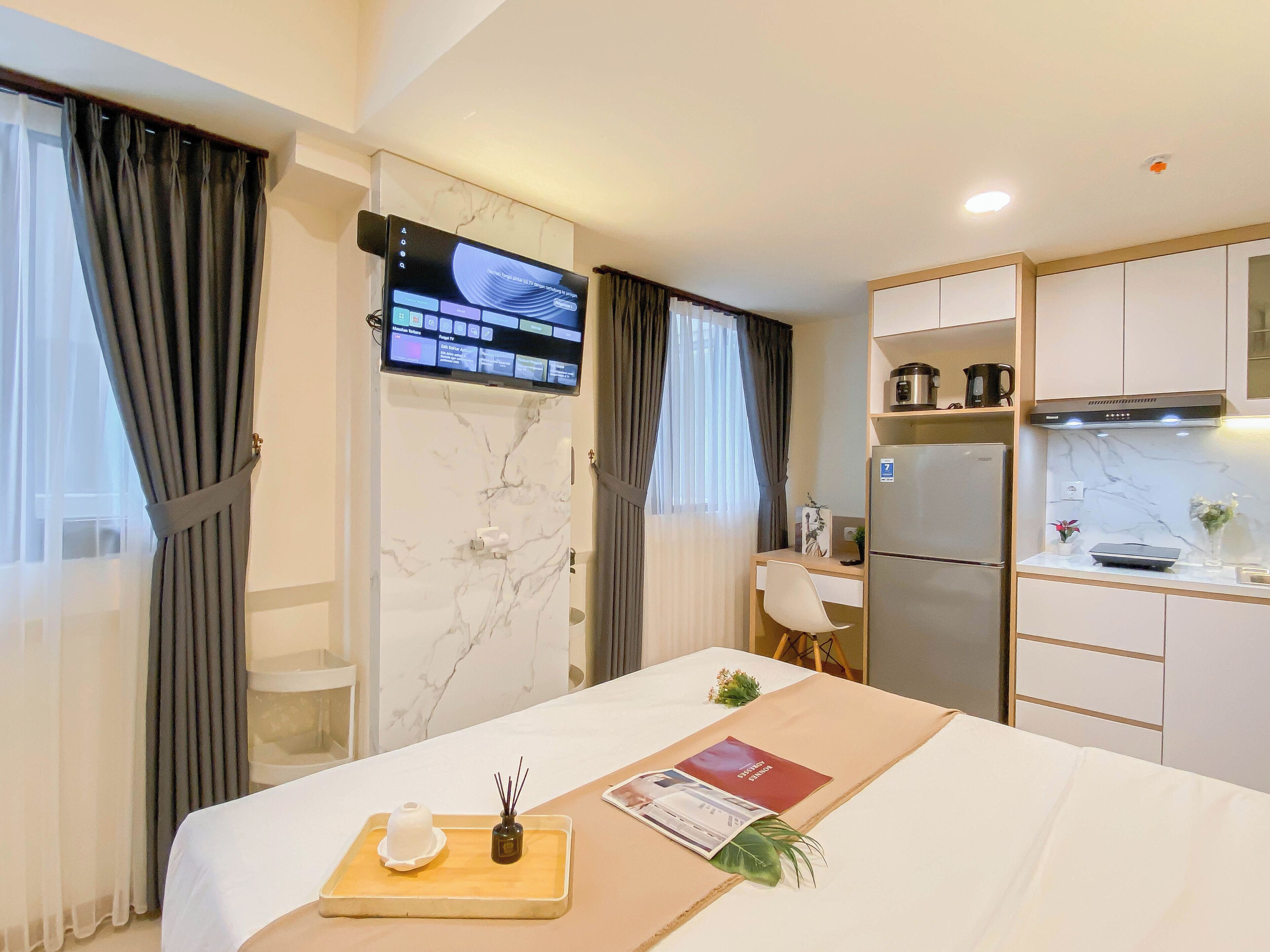 Une chambre d’hôtel moderne équipée d’un lit, d’un bureau, d’un téléviseur à écran plat, d’un coin cuisine avec réfrigérateur et four à micro-ondes, et de murs en marbre.