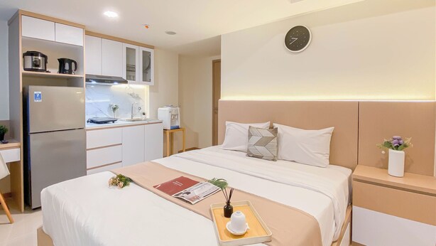 Una habitación de hotel moderna con cama, mesitas de noche, una kitchenette pequeña y un reloj en la pared.