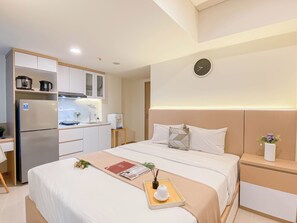 A modern hotel room with a bed, bedside tables, a small kitchenette, and a clock on the wall. - Simply Look Studio At Meikarta By Apartment Travelio (Cikarang)