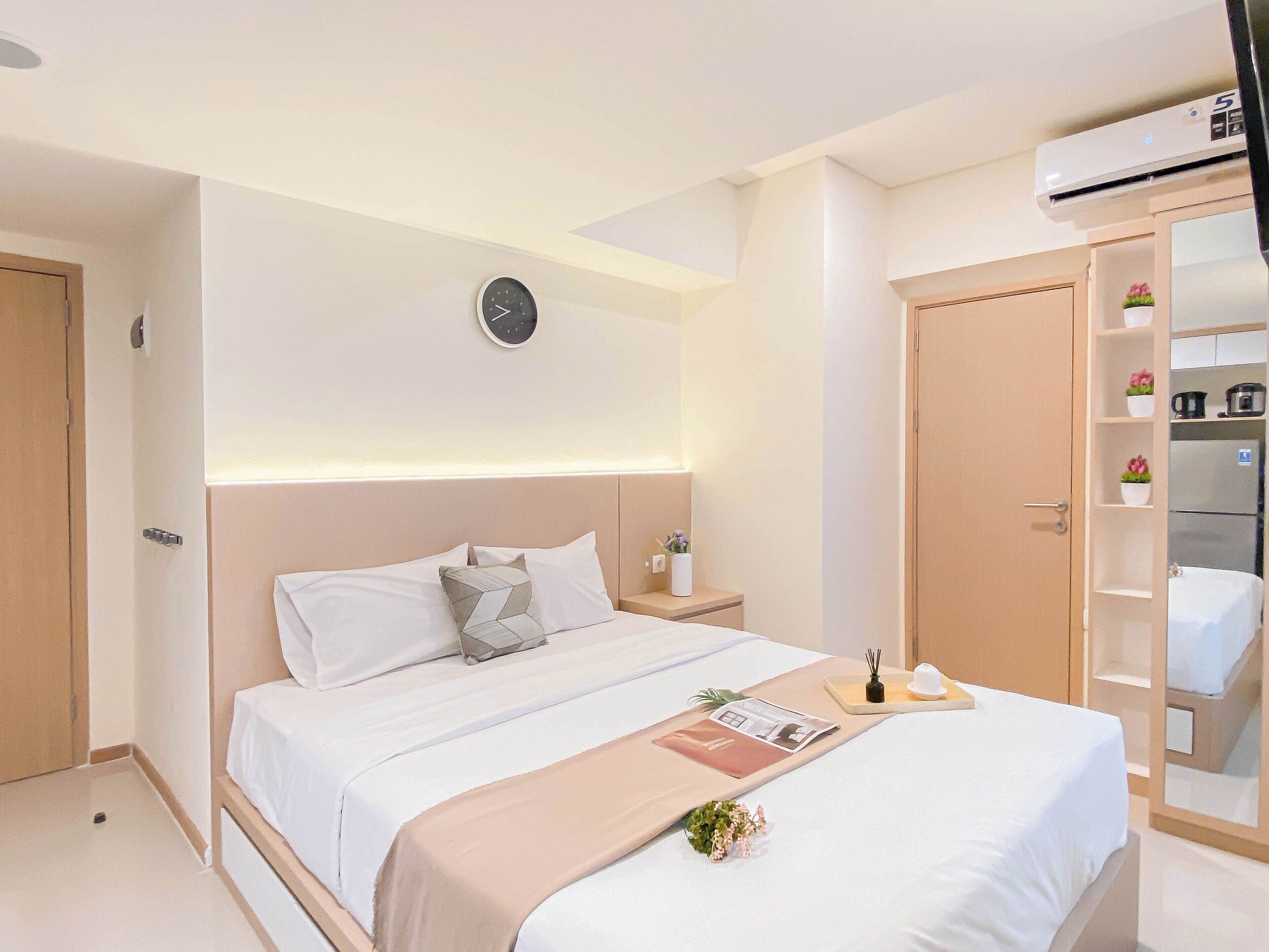 Une chambre d’hôtel comprenant un lit, une table de chevet, une horloge, une armoire et une petite plante.