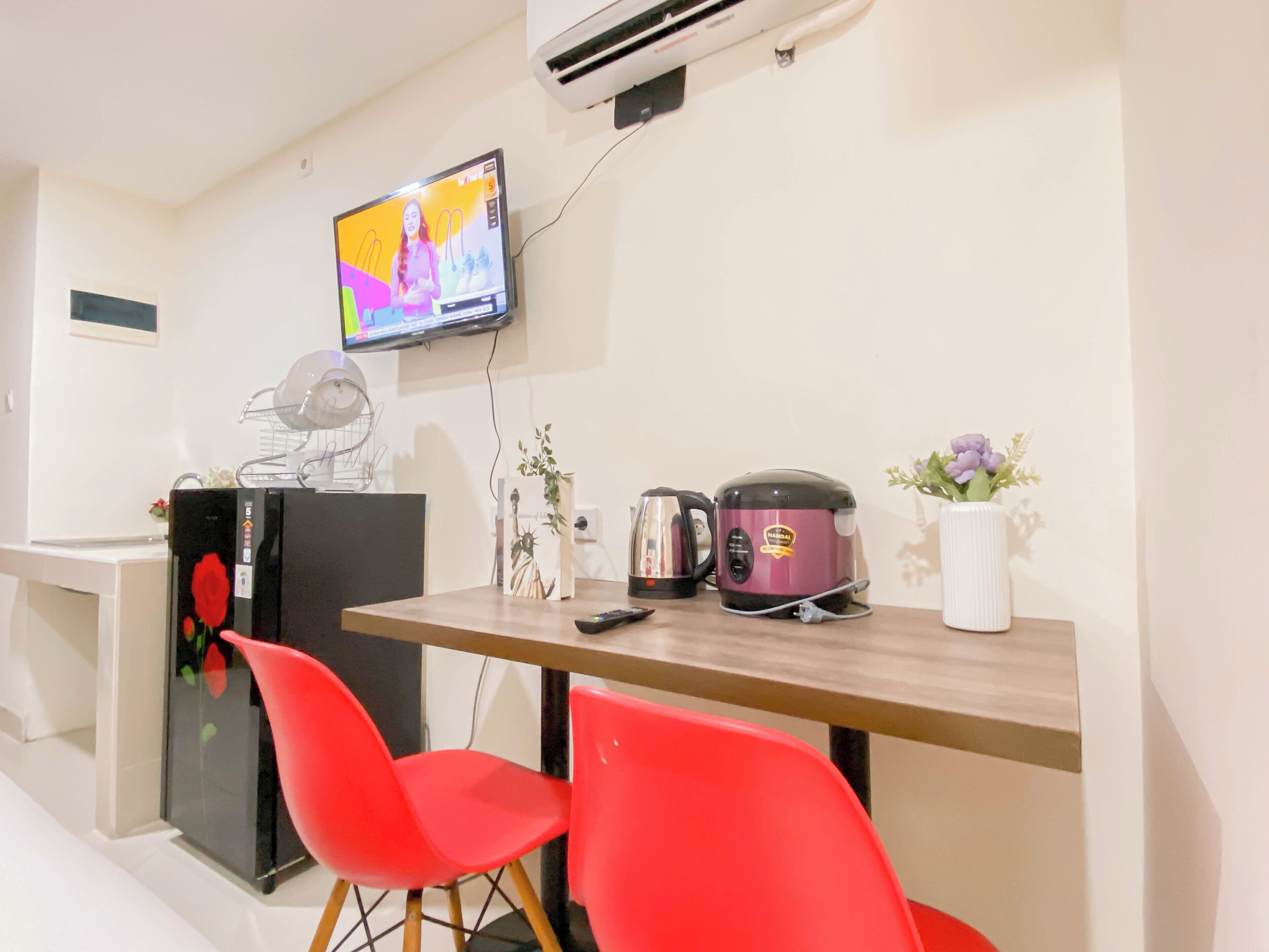 Una cocina moderna con televisor, una cocedora de arroz y sillas rojas.