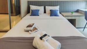 Et hotelværelse med en pænt redt seng, et lille natbord med en plante, og et skrivebord med stol.