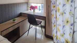 Et lille, moderne værelse med et skrivebord, en stol, en potteplante og et vindue med gardin.