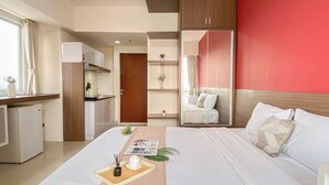 Une chambre d’hôtel équipée d’un lit, d’un bureau, d’une kitchenette et d’un mur d’accent de couleur rouge.