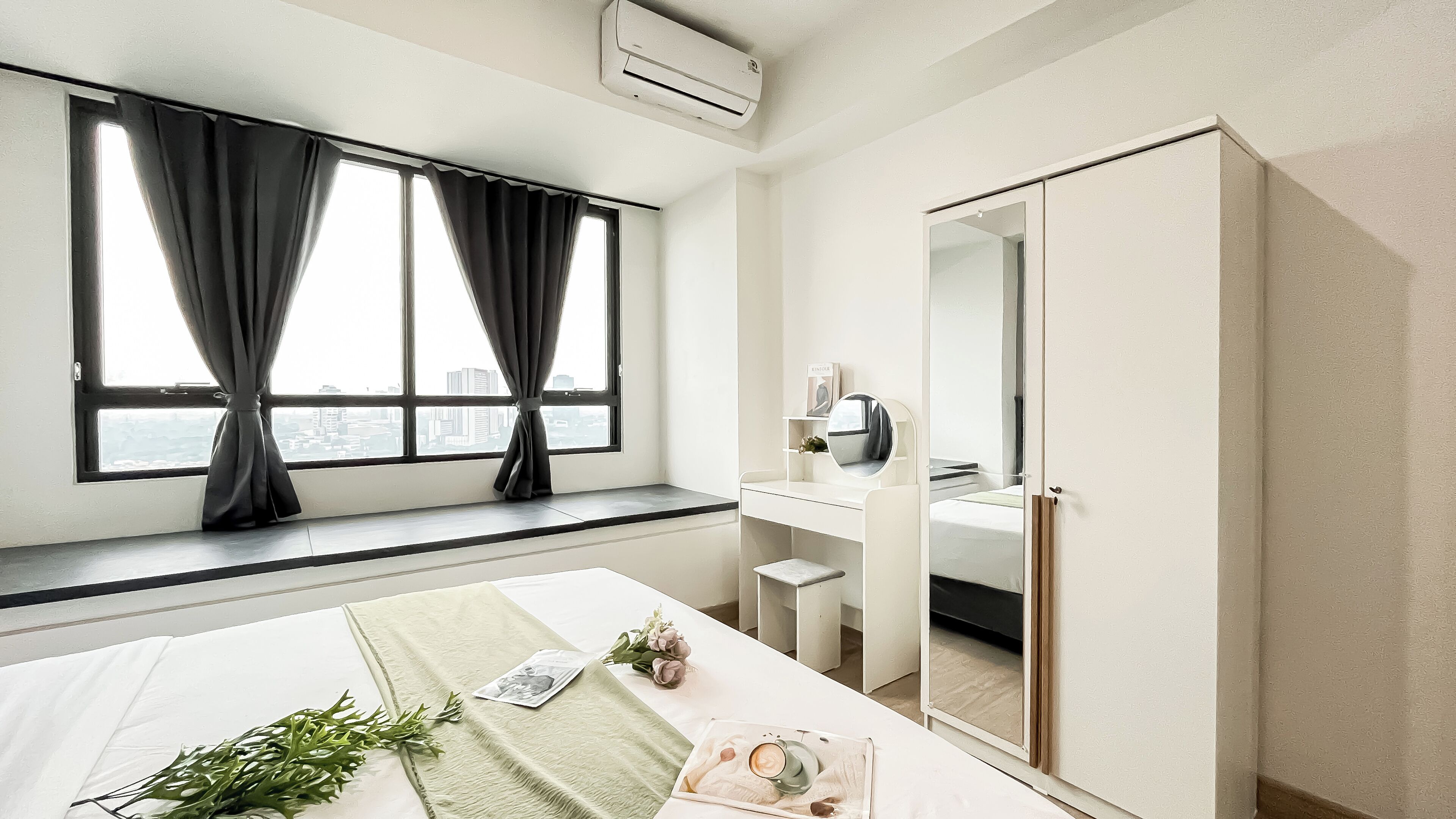 A hotel room with a bed, a desk, a mirror, and a window with curtains.