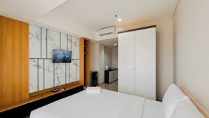 Une chambre d’hôtel comprenant un lit, un téléviseur fixé au mur, qui est décoré d’un motif imitant le marbre, une armoire en bois et un placard avec un miroir.