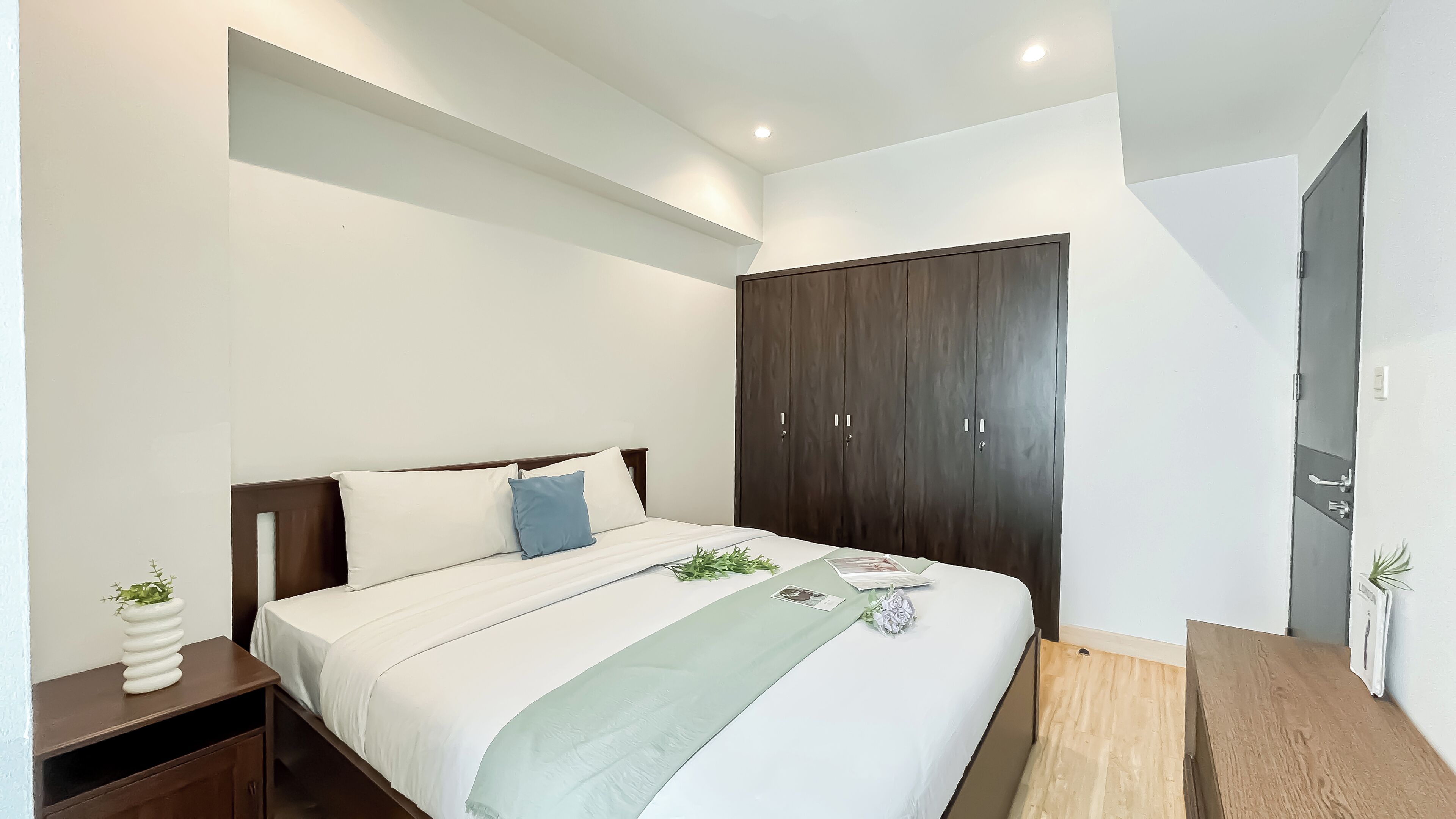 Une chambre à coucher avec un lit, une armoire en bois, des tables de chevet et une petite plante.
