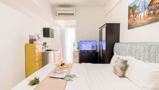 A hotel room with a bed, a desk with a computer, a TV, and a large window. - Basic Studio Near Station At Margonda Residence 2 Apartment (Depok)
