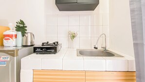 A modern kitchen with white tiles, a stainless steel sink, a Rinnai gas stove, a kettle, and a refrigerator. - Basic Studio Near Station At Margonda Residence 2 Apartment (Depok)