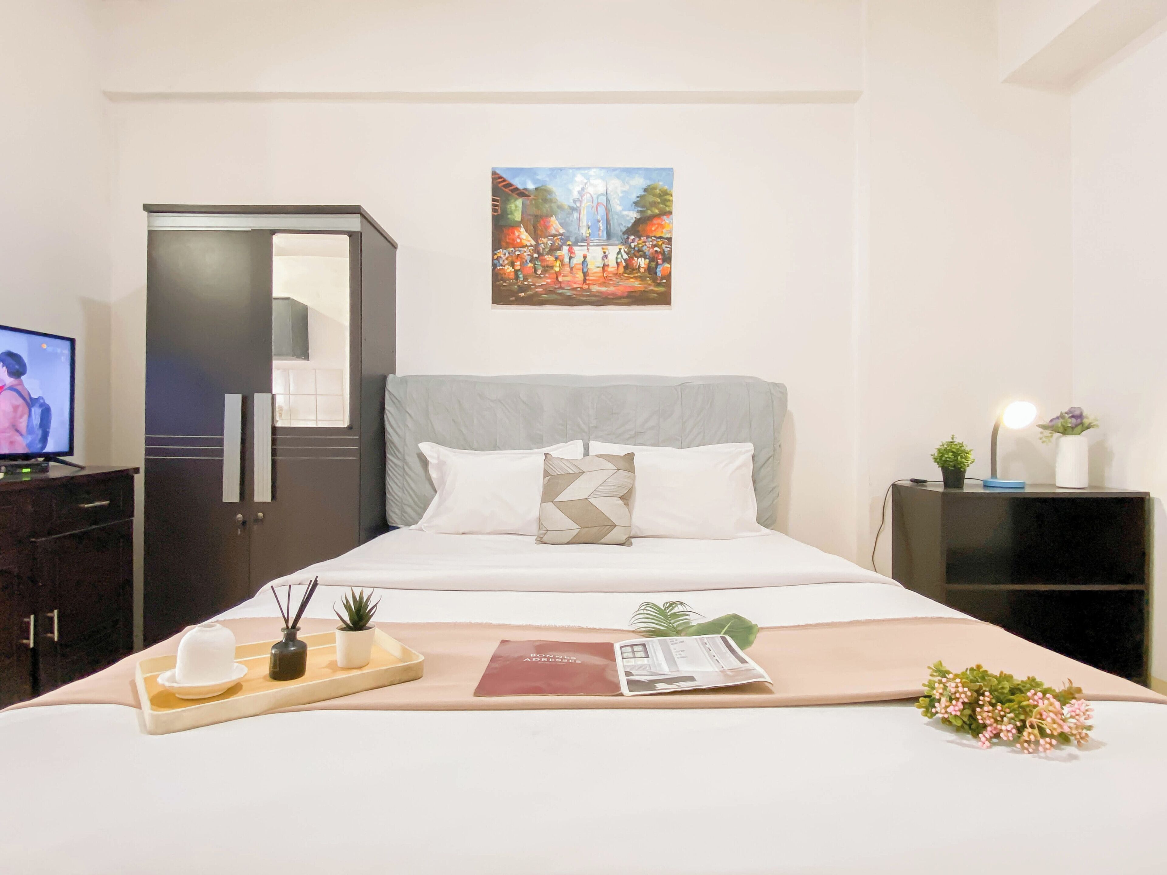 Een verzorgde hotelkamer met een bed, een nachtkastje met een lamp, een kleine potplant en een schilderij aan de muur.