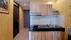 A modern kitchen with wooden cabinets, a black countertop, and a stainless steel sink. - Wooden Accent 2Br At Mekarwangi Square Cibaduyut Apartment (Bandung)