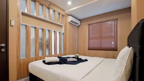 A bedroom with a bed, wooden paneling, an air conditioning unit, a window with blinds, and a door. - Wooden Accent 2Br At Mekarwangi Square Cibaduyut Apartment (Bandung)