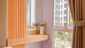 Una camera da letto con una finestra, uno scaffale con un vaso di fiori e un letto.
