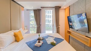 Una camera d'albergo con un letto, una TV a parete e una finestra con tende.