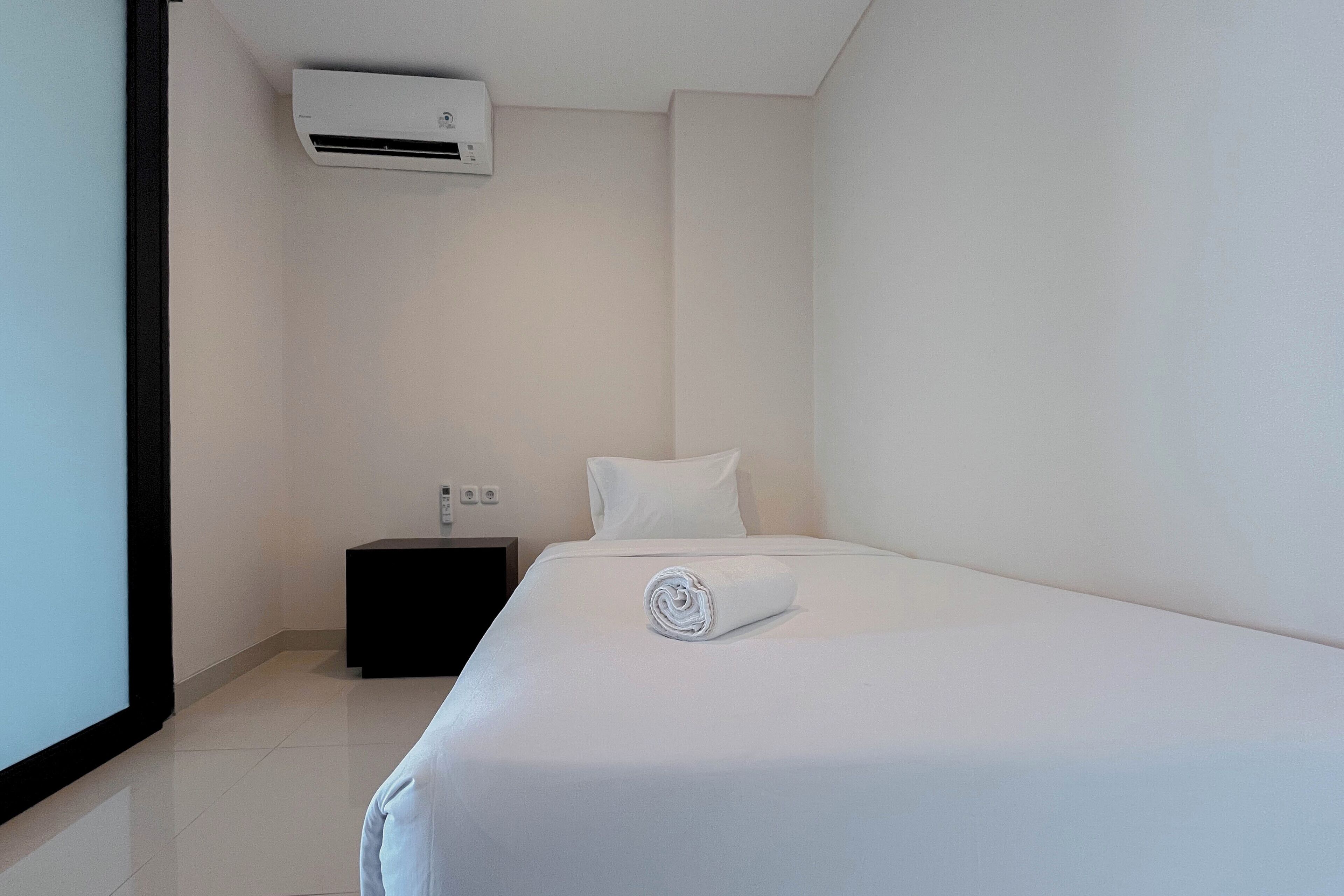 A hotel room with a neatly made bed, a small bedside table, and a wall-mounted air conditioner.