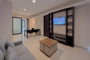 Ein modernes Wohnzimmer mit grauem Sofa, einem Holztisch, einem an der Wand montierten Fernseher und einem Essbereich mit Tisch und Stühlen.