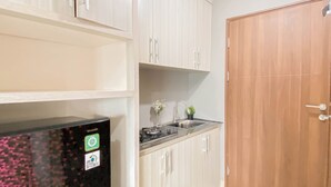 A compact kitchen with white cabinets, a stainless steel sink, and a black refrigerator. - Standard Studio Apartment At Lrt City Sentul - Royal Sentul Park (Bogor)