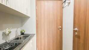 A compact kitchen with a wooden door, a sink, and a small potted plant. - Standard Studio Apartment At Lrt City Sentul - Royal Sentul Park (Bogor)