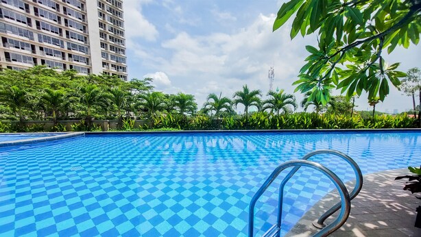 Une piscine à motifs en damier, entourée de verdure et avec un grand bâtiment en arrière-plan.