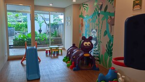 Un espace de jeux pour enfants avec un toboggan, des tabourets colorés et une fresque représentant des animaux de la jungle.