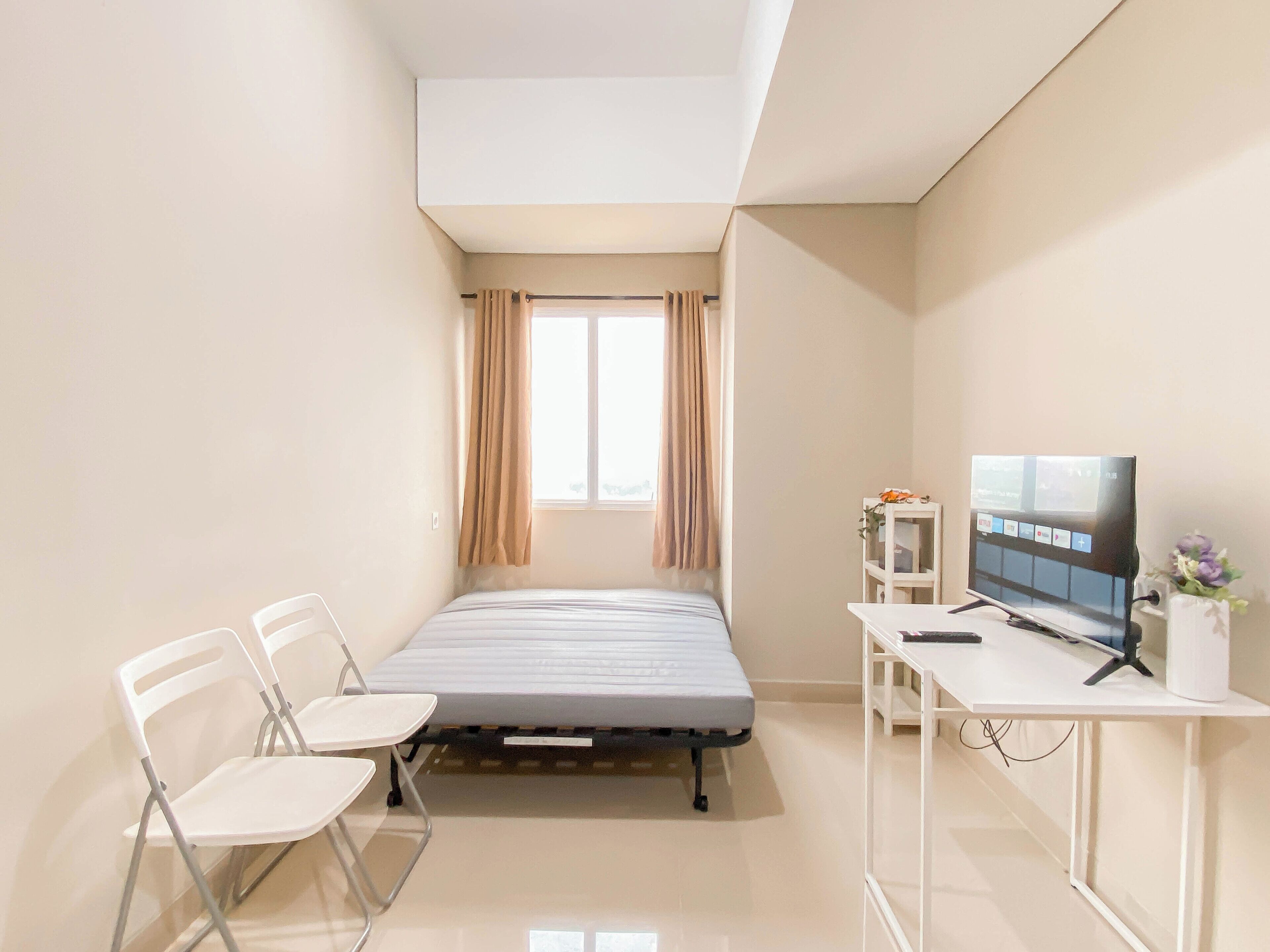 Une petite chambre moderne, équipée d’un lit, d’un bureau, d’une chaise et d’un téléviseur.