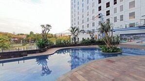 Une piscine dotée d’une terrasse en bois, entourée de plantes tropicales, et un grand bâtiment d’hôtel en arrière-plan.