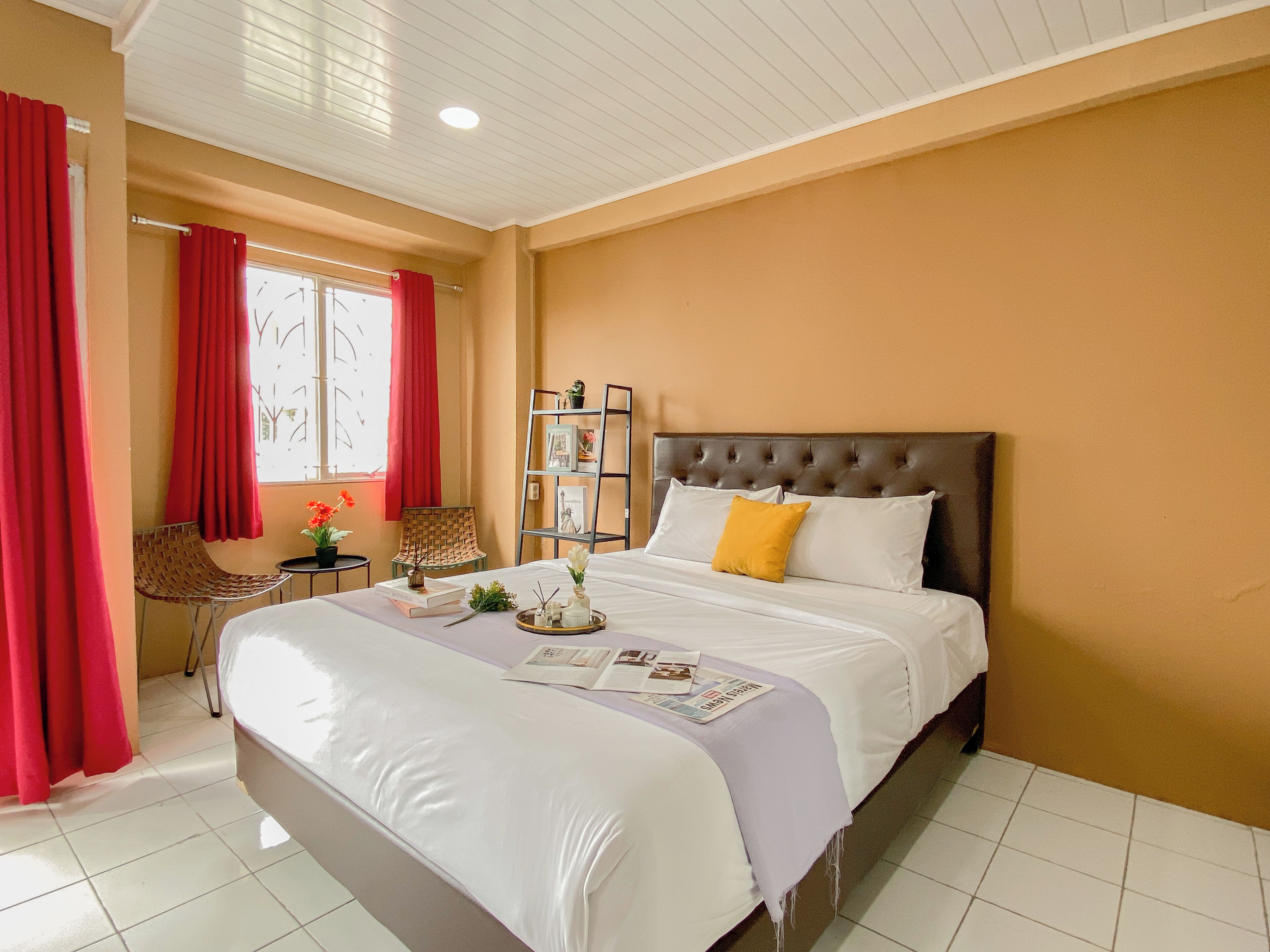 A neatly arranged bedroom with a large bed, a bedside table with a lamp, a chair, and a bookshelf.