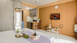 Moderni hotellihuone, jossa on sänky, pieni keittiönurkkaus, televisio ja kylpyhuone.