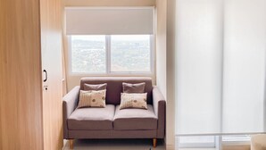 A room with a sofa, a window with a view, and a wardrobe. - Modern Style Studio Apartment At Royal Sentul Park (Bogor)