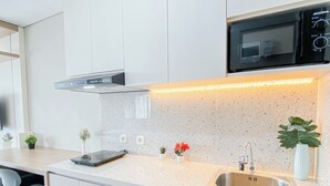 A modern kitchen with white cabinetry, a stainless steel sink, a microwave, and under-cabinet lighting. - Modern Style Studio Apartment At Royal Sentul Park (Bogor)