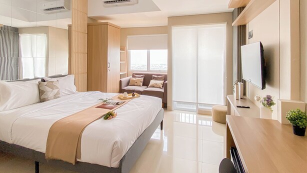 A modern hotel room with a large bed, a desk, a TV, and a balcony with a view. - Modern Style Studio Apartment At Royal Sentul Park (Bogor)